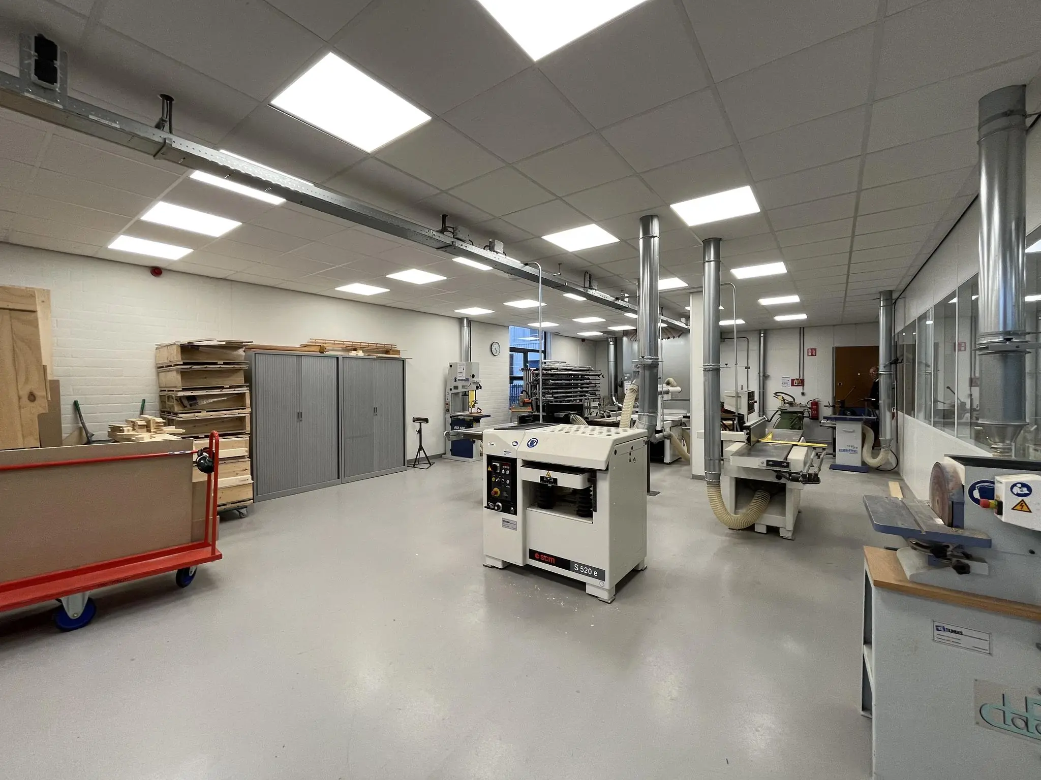 Moderne houtbewerkingsruimte aan de Niels Bohrweg met diverse machines, afzuigsystemen en opgestapeld houtmateriaal.